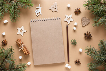 Craftbook, Notepad for wishes. Christmas background with wooden toys, fir branches, cinnamon sticks and marshmallows on a beige table. New year card. Copy space, mock up, flat lay, top view.