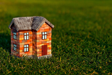 Brick toy house on the grass. Orange house on a green meadow. The concept of own housing and construction.