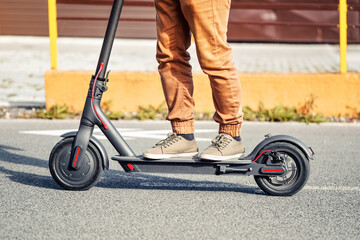 Young man in casual trousers riding an electric scooter detail on his feet and wheel over asphalt road © Lubo Ivanko