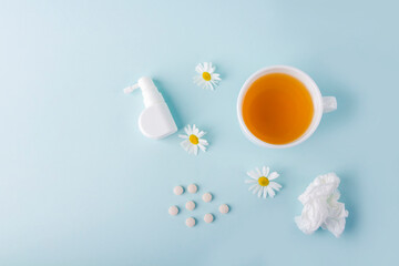 Cup of chamomile tea, spray for runny nose and crumpled paper wipes on blue background. Seasonal diseases and treatment of colds, flu, heat. Prevention of virus. Copy space for text