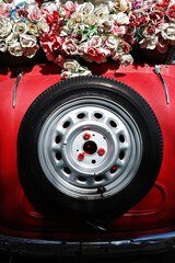 Classic old style of red car decorated by bunch of fake fabric flowers.