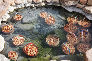 Big baskets of many eggs boiled under clear hot mineral water pond of hot spring.