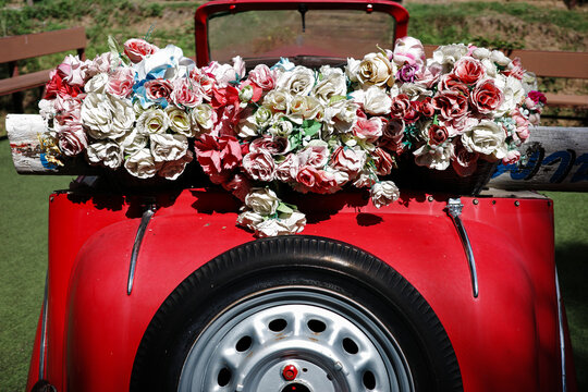 Classic old style of red car decorated by bunch of fake fabric flowers.
