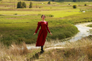 Young woman in vintage red dress standing in a valley of a river