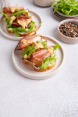 Bruschetta with prosciutto and arugula on a plate. Light background