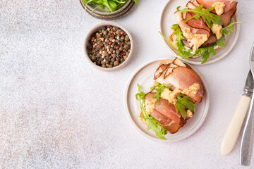 Bruschetta with prosciutto and arugula on a plate. Light background