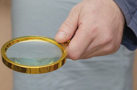 An adult male holds a magnifying glass in his hand. A large roun
