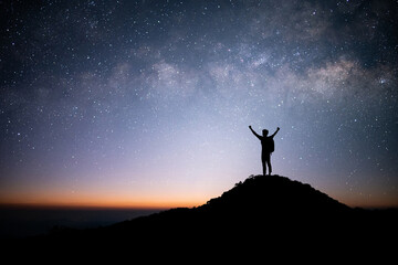 Silhouette of young traveler and backpacker standing and open arm and watched the star and milky way alone on top of the mountain. He enjoyed traveling and was successful when he reached the summit.