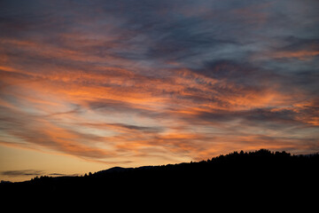Fototapeta na wymiar Brennender Himmel mit rot orangen Wolken und Sonnenuntergang mit Bergpanorama als Scherenschnitt im Vordergrung
