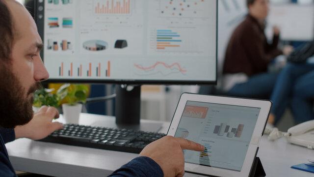 Paralysed business man sitting immobilized in wheelchair working at tablet and computer in same time analysing financial graphs, pc showing data prosessing on display for project regarding economy