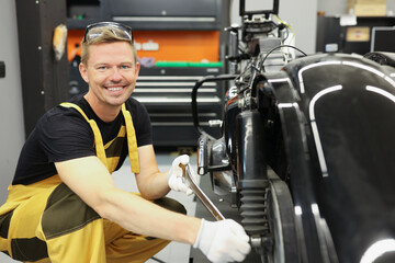 Smiling mechanic spinning motorcycle wheel with wrench in work shop