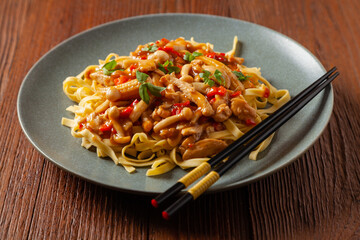 Traditional noodles with shimeji mushrooms and chicken. Prepared in a wok. Served on a gray plate.