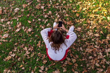 beautiful young woman using a smartphone sitting in the grass in autumn