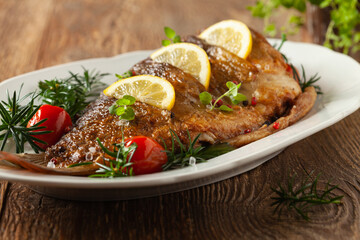 Fried carp whole. Served with lemon and cherry tomatoes on white plate. Christmas decoration.