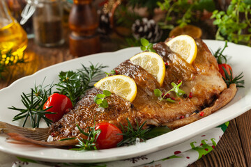 Fried carp whole. Served with lemon and cherry tomatoes on white plate. Christmas decoration.