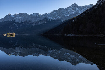 Symmetrisches Bild eines Bergpanoramas mit ieinem Bergsee und einer kleinen Insel die gerade noch von den letzten Sonnenstrahlen des Tages in Licht getaucht wird. Die Zugspitze im Hintergrund.