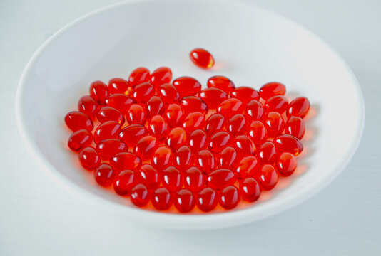 A Plate Full Of Red Soft Gel Capsules Of Gac Oil Or Momordica Cochinchinensis Oil In White Background