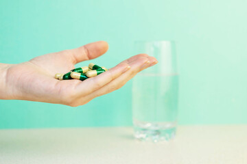  woman's hand holds a handful of green pills on green background with glass of water. Pharmacy or health care concept. Copy space