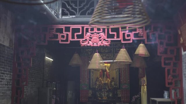 China spiral joss sticks burn hanging near Buddha statue in decorated ancient temple. Traditional Asian spiritual rituals and culture