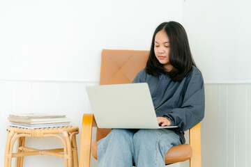 Portrait, a cute Asian teenage girl. wearing gray shirt studying online with notebook computer in bed in the bedroom happily