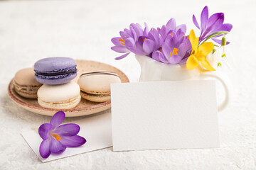 White paper business card mockup with spring snowdrop crocus flowers and multicolored macaroons on gray concrete background. side view, copy space.