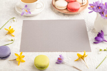 Beige paper sheet mockup with spring snowdrop crocus flowers and multicolored macaroons on gray concrete background. side view, copy space.