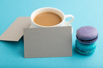 Gray paper business card mockup with blue and violet macaroons and cup of coffee on blue pastel background. side view, copy space.