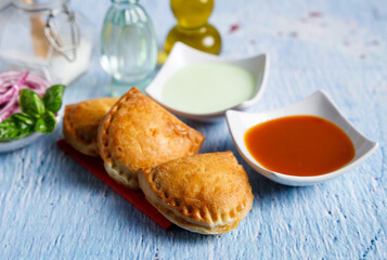 Fototapeta na wymiar Homemade empanadas with sauces. South American street food. These delicious beef empanadas are mandatory to eat, they have a crunchy dough and an exquisite ground beef filling.