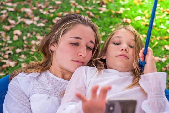 two sisters in a swing in autumn using a smartphone together