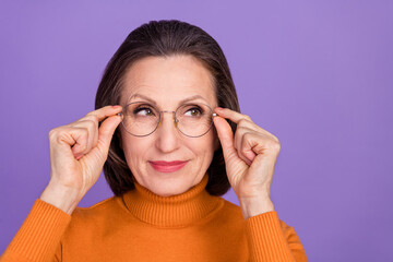 Photo of cute thoughtful lady pensioner dressed orange turtleneck arms glasses looking emty space smiling isolated purple color background