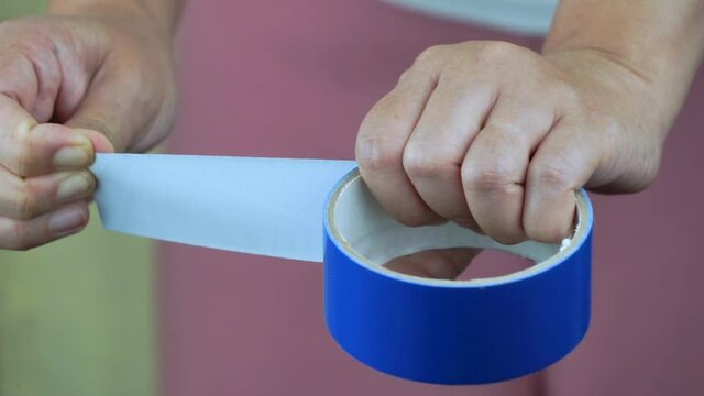 Hand pulling roll of duct tape, woman tears off a piece of duct tape. Parcel packing process.