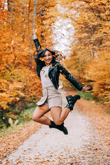 Cute girl smiling, jumping and playing with the leaves in the woods during the autumn season.