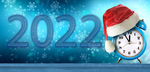 alarm clock and red christmas hat on winter abstract blue background