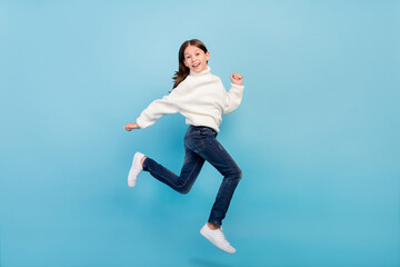 Fototapeta na wymiar Photo of adorable funky preteen girl dressed white pullover running fast jumping high smiling isolated blue color background