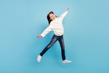 Fototapeta na wymiar Photo of excited sweet preteen girl dressed white pullover jumping high arms sides smiling isolated blue color background