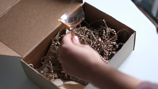 woman opens a delivery box from a store and discovers a broken glass. An improperly packed item crashed on delivery