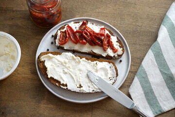 Sandwiches with cream cheese and dried tomatoes in a plate on a wooden table.