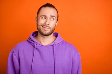 Photo of unsure millennial brown tail hairdo guy look empty space wear purple hoodie isolated on orange color background