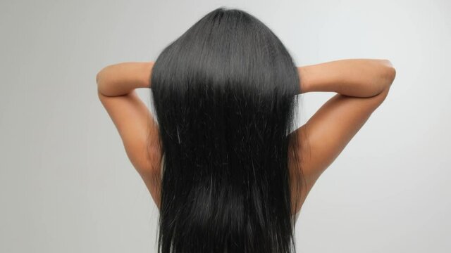 Brunette with luxurious hair on a white background in the studio. The girl pulls her hair. Hair care cosmetics.