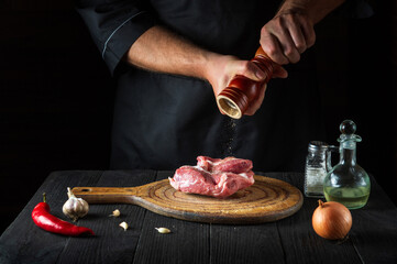 Cook cooking raw meat fillet and adding pepper or chili for marinade. Working environment in kitchen in restaurant or cafe