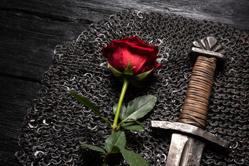 Red rose flower and knight sword on the black table background.