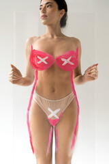 Woman holding transparent glass with x symbols at breast and bikini zone and looking away