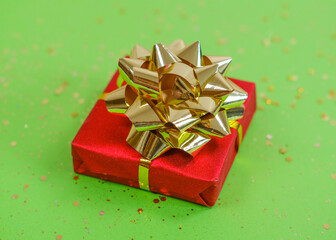 Red gift box with golden ribbon on the green background with golden sparkles.