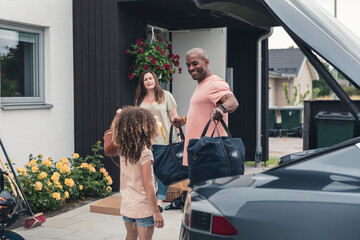 Smiling father looking at daughter while loading luggage in electric car