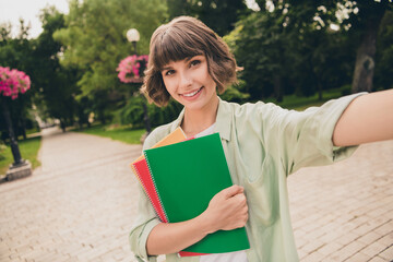 Photo of dreamy sweet young woman wear green shirt smiling embracing copybooks tacking selfie...
