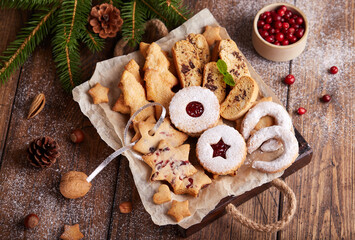 Box with variety of Christmas cookies: linzer cookies with jam, stars with cranberries, Christmas trees with brown sugar, Biscotti cantucci with almonds and chocolate, horseshoe with sugar powder - obrazy, fototapety, plakaty