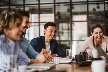Smiling businessman looking away while sitting amidst cheerful colleagues at conference table