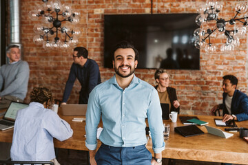 Portrait of happy male professional standing while colleagues discussing in background