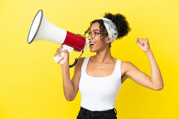 Young african american woman isolated on yellow background shouting through a megaphone to announce something in lateral position