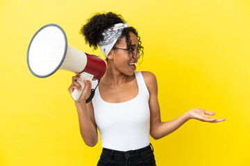 Young african american woman isolated on yellow background holding a megaphone and with surprise facial expression